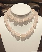 Two strands of pale pink irregular rose quartz beads displayed on a white necklace stand, showing the size and clarity of the beads.