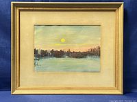 Full view of the framed watercolour landscape painting with a yellow sun above a horizon of tree silhouettes and a field.