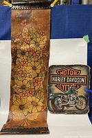 Photo showing both leather wall hangings: a large floral tapestry and a smaller Harley Davidson motorcycle logo piece