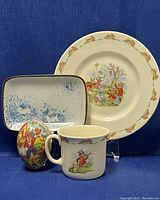 Image showing the 8-inch Bunnykins plate, matching mug, hand-painted hollow Easter egg, and small ceramic tray with bunny designs on blue background