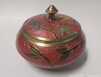 Side view of the vintage brass and enamel covered jar showing the floral enamel decoration and brass lid with knob.