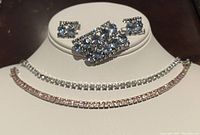 Vintage Continental crystal costume jewelry set displayed on stand, showing brooch, earrings, and two tennis bracelets with clear and pinkish stones.