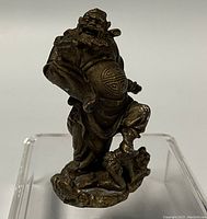 Photo showing diagonal side angle of the miniature brass Asian warrior statue on a clear stand.