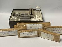 Photo showing several shiny metal rectangular print blocks placed inside a box with several labeled paper-wrapped packages.