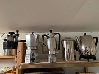Five coffee makers displayed in a row on a shelf