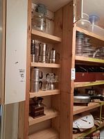 Shelf containing various coffee making equipment including a glass coffee pot, metal coffee pots, and a wooden coffee grinder.
