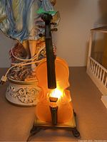 Front view of amber glass cello lamp illuminated on a table, showing detailed neck and strings.