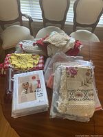 Overview of assorted linens on a table including packaged and loose linens with lace and floral patterns, sunflower fabric, and others