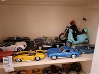 Shelf with seven Maisto model vehicles including cars and a motorcycle model with rider figure