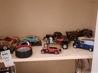 Shelf view showing multiple vintage style model cars and a tire style clock alongside them.