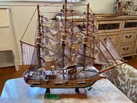 Full view of the model ship on a wooden base from the side, showcasing the sails and rigging.