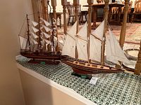 Photo showing two wooden model ships with cloth sails on a patterned shelf.