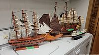 Wide view showing five handmade wooden model ships on display, varying styles and sizes including multi-masted sailing ships and a modern ship model