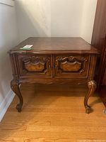 Front view of vintage wooden side table showing carved details and two cabinet doors.