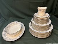Stacked and grouped photo showing all plates stacked in three sizes, serving bowl, and cup with plate on a dark cloth background.