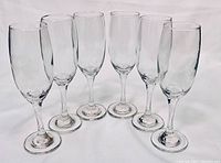 Photo of six clear glass champagne flutes arranged on a white surface showing their shape and size.