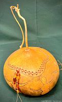Full side view of the gourd showing the etched designs, the sewn lacing, bead embellishments, and the curved stem handle.