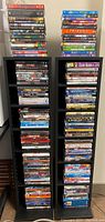 Two black DVD towers filled with many DVDs organized vertically and stacked, showing diverse genres.