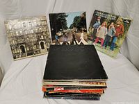 Front view of a stack of vinyl records including The Beatles - Abbey Road, Led Zeppelin - Physical Graffiti, The Mamas & The Papas - 6 Of Their Greatest Hits, and AC/DC - Back in Black