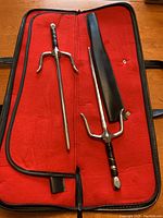 Two metal sai weapons placed inside the open carrying case with red fabric interior.
