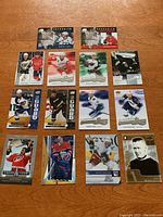 Full view of 14 hockey cards laid out on wooden table, showing various players including Gretzky, Vezina, Ovechkin. Mix of insert and base cards with different designs and backgrounds.