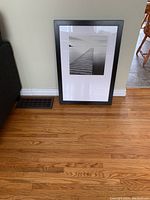 Framed dock print standing on the floor showing full frame and mat with black and white image.