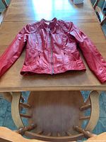 Red leather women's jacket laid flat on a wooden table, showing front view with zipper closed and detailed seams.