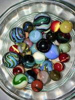 Group of 50 Jabo marbles displayed in a container, showing various colors, sizes, and swirl designs.