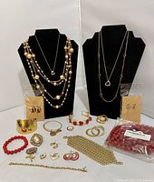 Full lot showing necklaces on black display stands, earrings in packets, bracelets, pins, and ring laid out on surface.