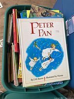 Overhead photo of a green bin filled with various children's books including 'Peter Pan' on top.