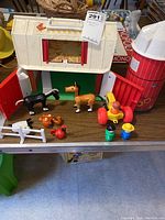 Wide view of Fisher Price barn play toy, red silo, animals and figures arranged on a table.