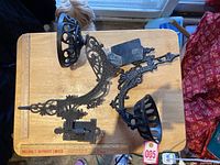 Two black cast iron antique wall brackets arranged on a wooden surface showing the detailed scrollwork and semi-circular lamp holders