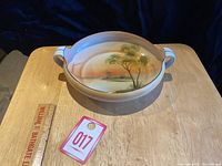 Top-down and angled view of the hand painted Nippon bowl showing the handles and scenic painted landscape inside the bowl.