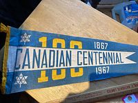 Full view of blue felt pennant with '100', 'Canadian Centennial', and '1867-1967' text and geometric maple leaf designs.