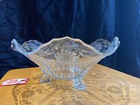 Side view of footed clear glass bowl showing cornflower floral pattern and three decorative feet.