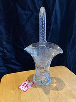 Image showing full view of clear crystal basket vase with high handle and scalloped rim on wooden surface
