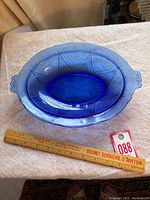 Top view of blue Depression glass oval bowl with ruler showing 11 inches length, embossed pattern visible inside bowl.