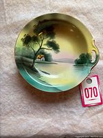 Photo of the round handled dish with hand-painted landscape scene showing house, trees, and water.