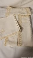 Folded vintage white linen tablecloth and napkins showing lace trim detailing on a cream background