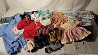 Wide view displaying all assorted doll and infant clothing including jackets, dresses, hats, and footwear spread on white surface