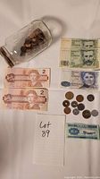 Overview photo showing Canadian two-dollar bills, Spanish pesetas coins and banknotes, pennies in a jar, and an unidentified banknote.