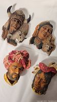 Four vintage wall plaques displayed on a white background, showing detailed hand painted faces of Native American figures and a turbaned male.