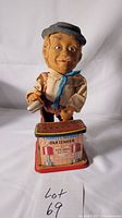 Front view of Charley Weaver bartender tin toy on bar base showing figure and printed bar sign with shaker in hand.