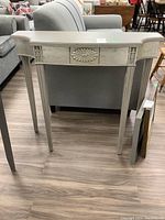 Front view of painted wood accent table showing decorative floral carving.