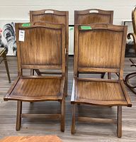 Four foldable wood chairs with slatted back and seat, warm brown finish, light wear visible.