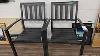 Two black metal chairs side by side with slatted seat and back, straight armrests, visible scratches.