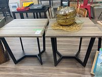 Two square end tables side by side showing the metal base with a geometric design and wood-look tops in light gray wood grain covered with plastic-like laminate.