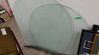 Two large round clear glass table tops leaning against a wall, one about 45 inches and another about 37 inches with some minor surface marks visible.