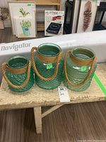 Full view of the three green glass jars with rope handles placed on a wooden bench, showing their sizes and textures.
