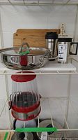 Photo of two shelves showing three wooden Emeril Lagasse cutting boards, Jamie Oliver stainless steel pan with lid, one thermos, kitchen décor spoon stick labeled 'Mom's Kitchen', and another travel thermos bottle.